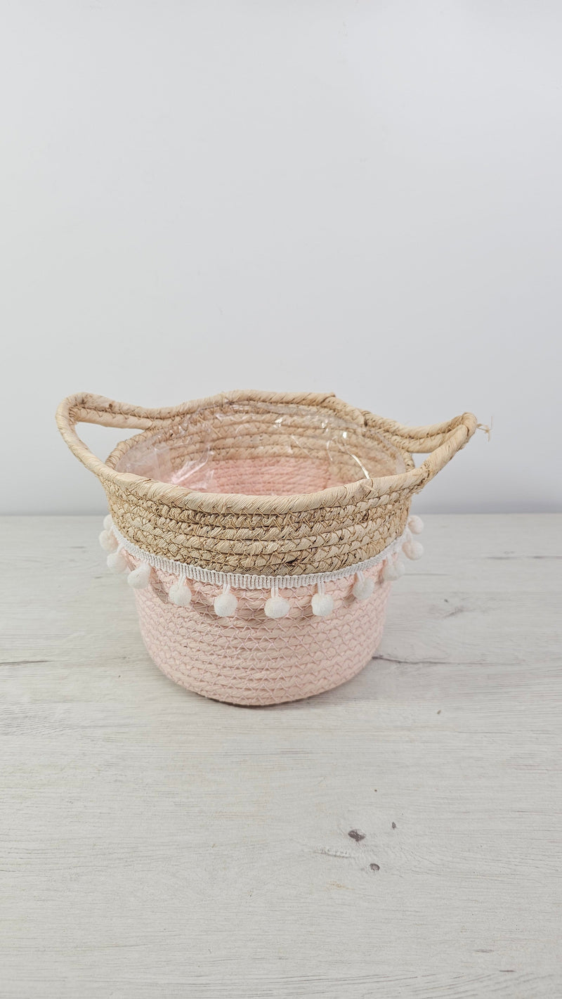 Cubremacetas tipo cesta rosa con pompones y asas de fibra natural