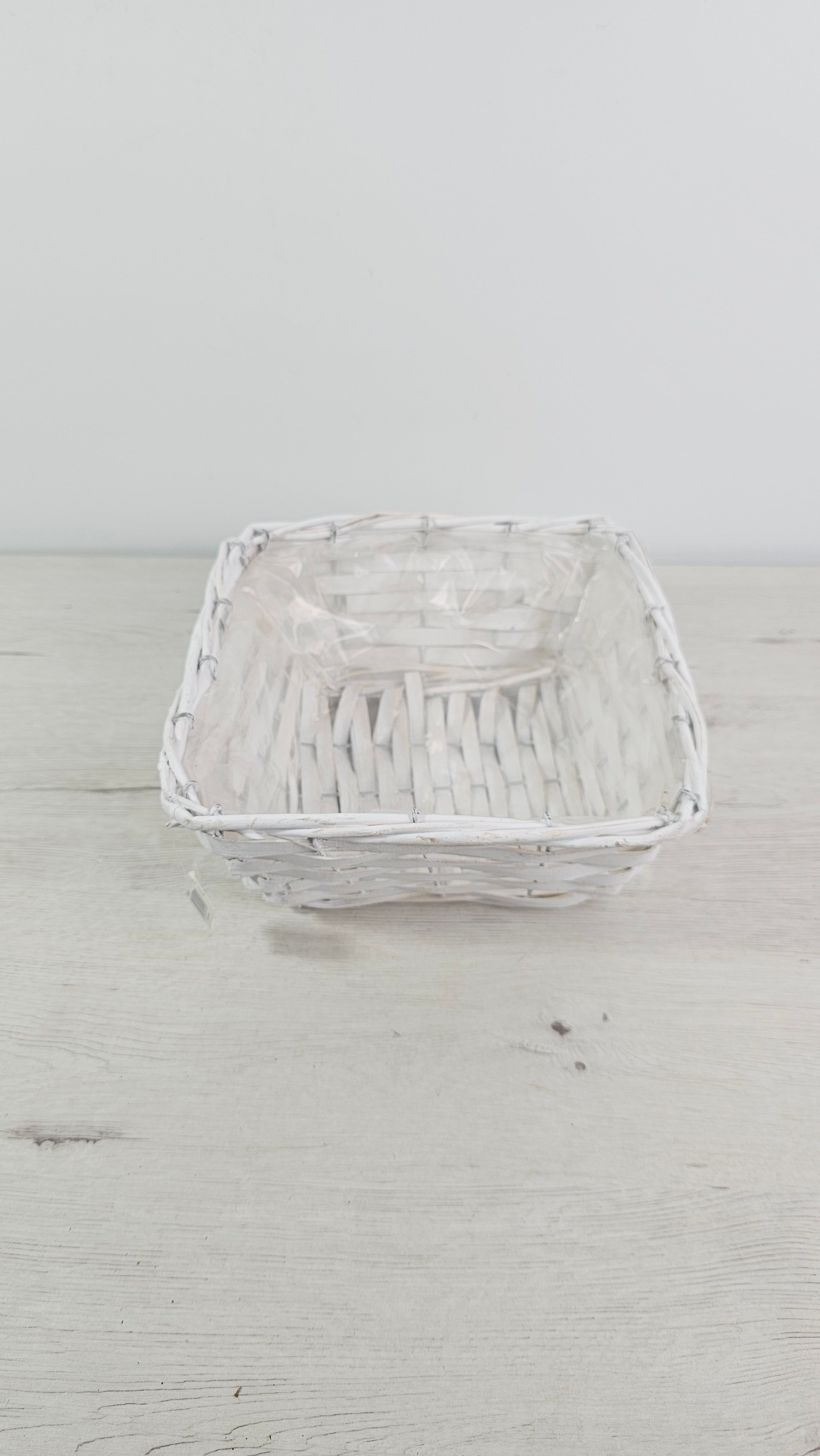 Cesta blanca cuadrada usada como cubremacetas para una planta de interior.