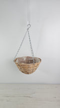 Cesta colgante de fibra natural tipo mimbre para usar como macetero decorativo.  