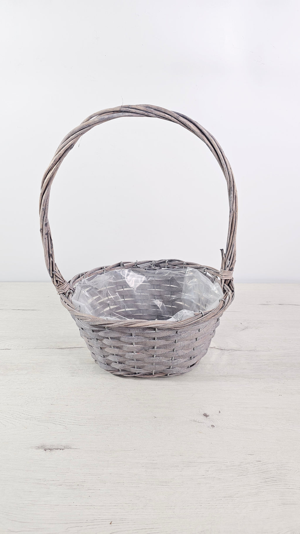 Cesta gris con asa alta y forro interior de plástico para plantas y regalos.  