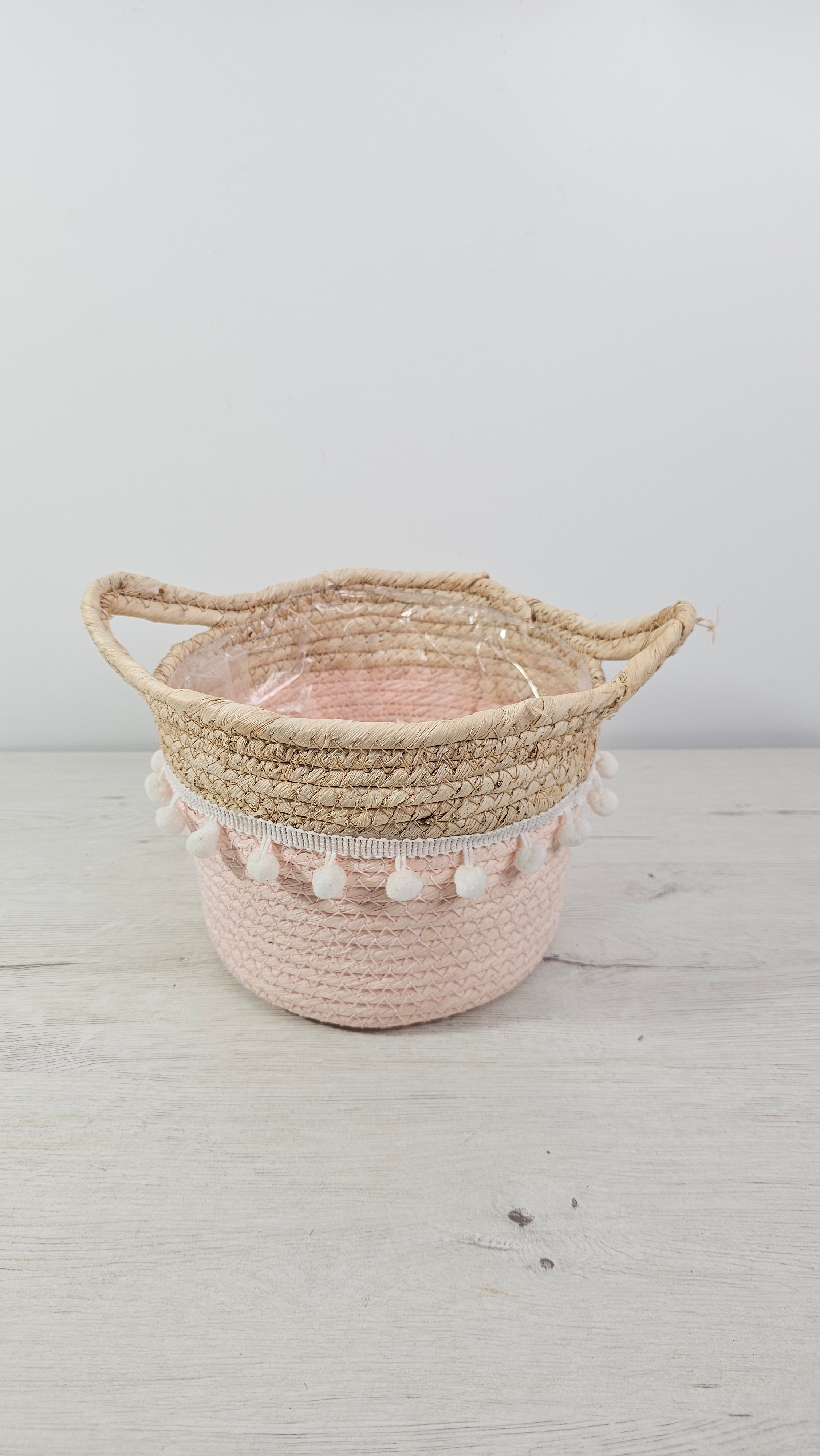Cubremacetas tipo cesta rosa con pompones y asas de fibra natural