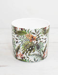 cubremacetas tropical de cerámica con fondo blanco y estampado de hojas y flores verdes.