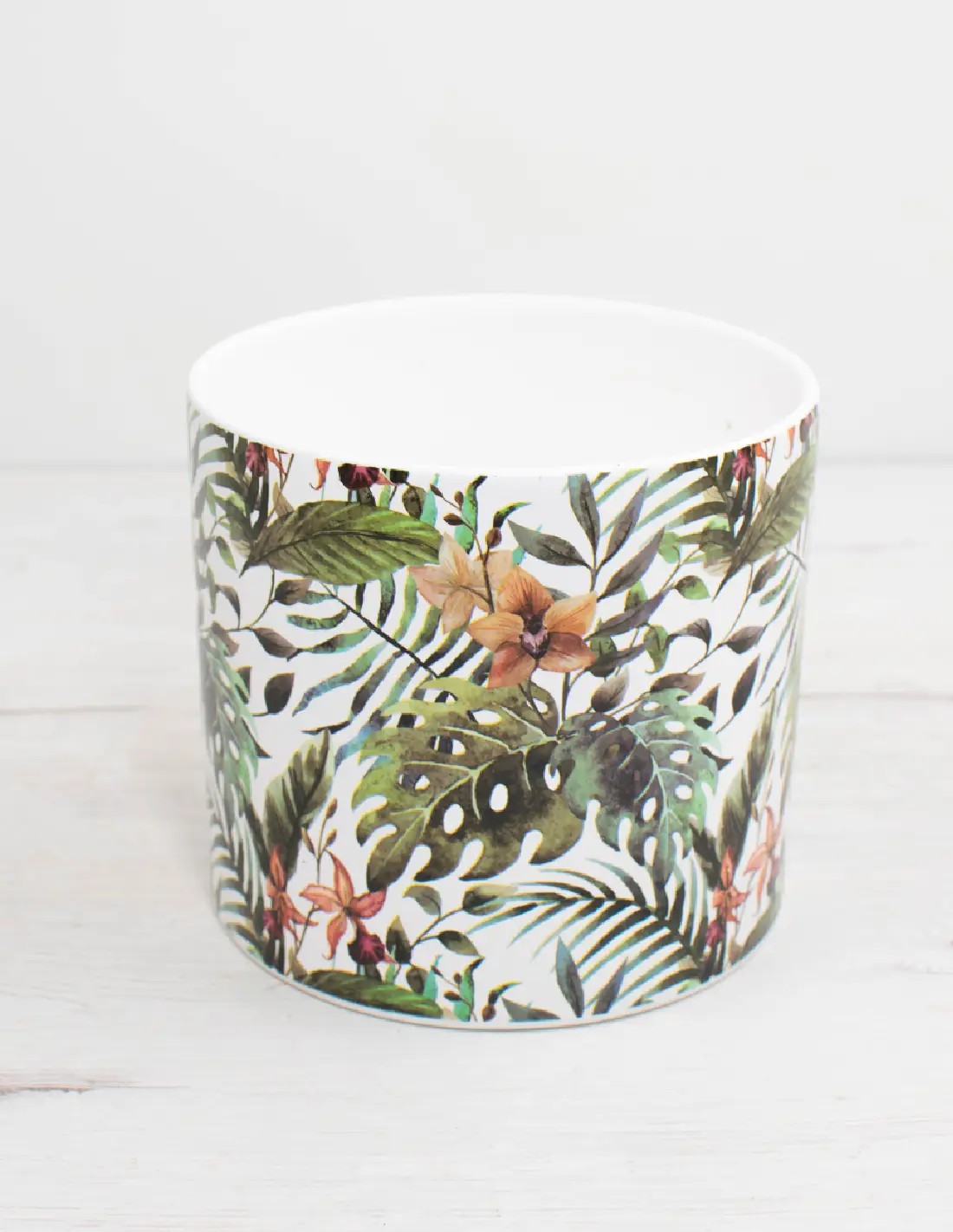 cubremacetas tropical de cerámica con fondo blanco y estampado de hojas y flores verdes.