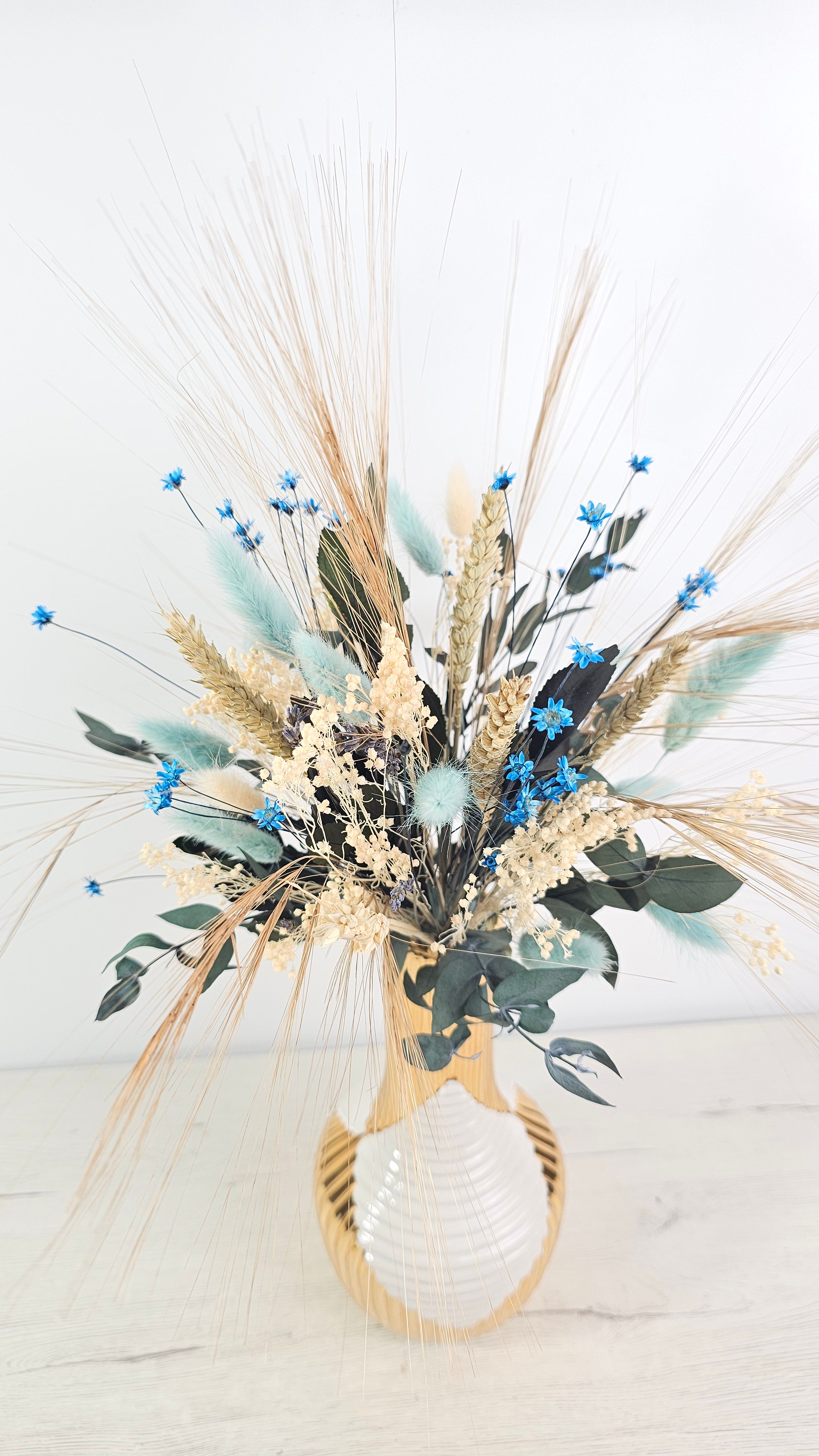 Centro decorativo de flores secas con pequeños detalles azules y espigas naturales.  